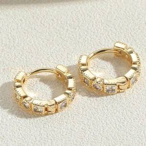 Macro shot of gold-plated earrings featuring clear square zircons on textured background