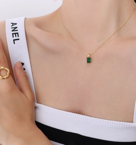 Dettaglio della collana dorata con zircone smeraldo e anello ondulato sulla modella
