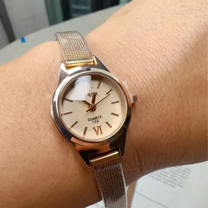 Detailed close-up of a rose gold quartz watch with a milanese mesh strap on a female wrist