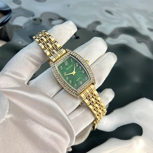 Detail of tonneau gold watch with emerald dial and diamond bezel held by gloved hand
