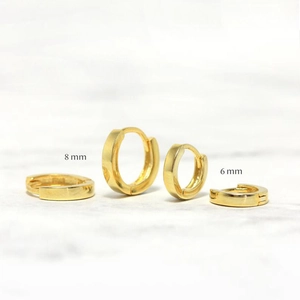 Close-up of gold S925 sterling silver hoop earrings in 6mm and 8mm sizes over marble