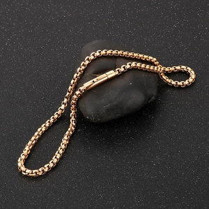 Macro shot of gold box chain necklace with push-pull clasp on dark stone surface
