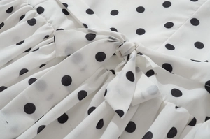 Détail d'une robe blanche à pois noirs avec un nœud délicat sur le tissu léger