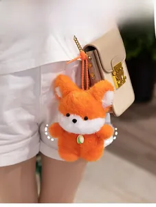 Detail of fox plush keychain with green bell and golden chain on beige leather bag