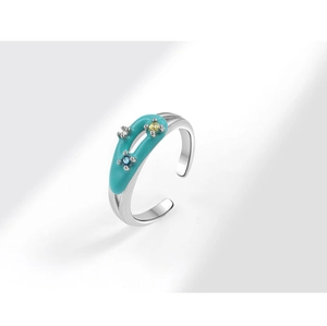 Detail of silver open ring with blue enamel and three colored gemstones on white base