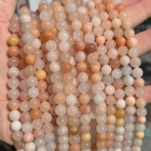 Close-up of hand-held natural round stone beads in orange and pink gradient tones