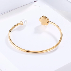 Close-up of golden open bangle featuring a white pearl and a stylized metal flower accent