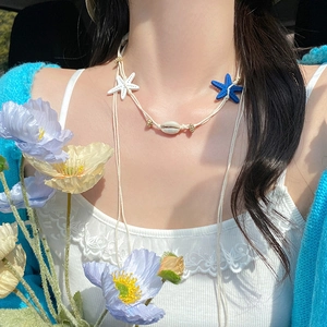 Détail d'un collier de plage avec étoile de mer bleue, coquillage et cordon tressé sur modèle