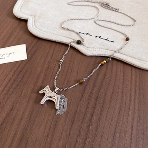 Silver pony pendant necklace with metal tassels and brown beads on a wooden desk