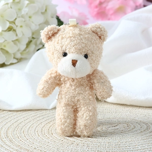 Close-up of beige teddy bear plush pendant with curly faux fur texture and pink blush