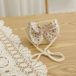 Détail d'un sac bandoulière en paille pour enfant avec nœud floral et bordure en dentelle