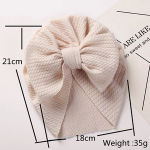 Pink ribbed baby turban hat with oversized bow and size measurements in a flat lay view