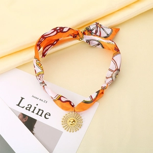 Détail du collier foulard en soie avec pendentif soleil doré sur fond de satin