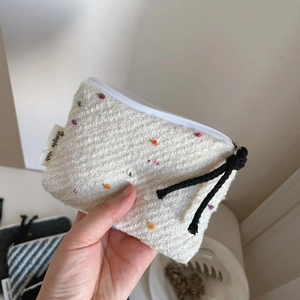 Macro dettaglio di un portamonete in tweed crema con puntini colorati e zip