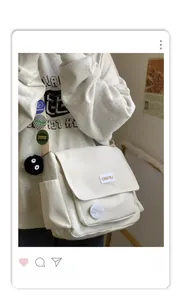 Detail of cream messenger bag with colorful badges and a black plush charm on the strap