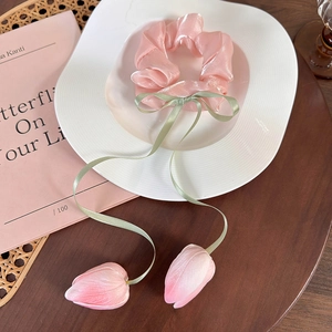 Detail of pink tulip scrunchie with green ribbons on a white plate and wooden table