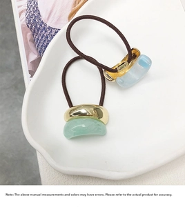 Detail of elegant U-shaped hair ties with green and blue resin stones on a ceramic plate
