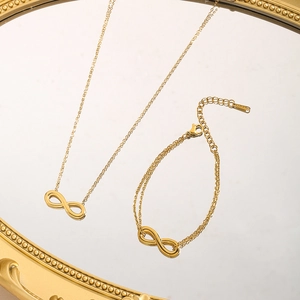 Golden infinity symbol necklace and bracelet set on a mirror for minimalist jewelry styling