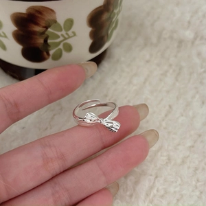 Detail of silver bow knot open ring worn by model against a cozy vintage background