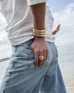 Nahaufnahme eines goldenen breiten Armreifs und eines strukturierten Rings am Strand