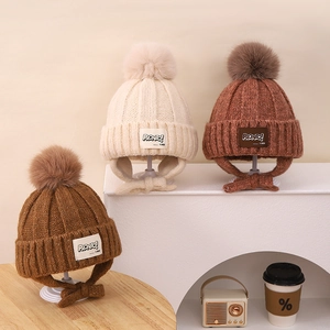 Close-up of three knit earflap hats in beige and brown with fluffy pom-poms and straps