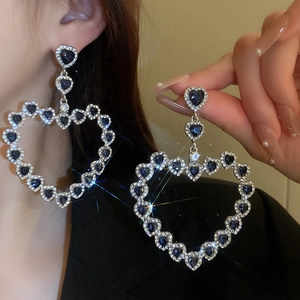 Exaggerated silver needle earrings featuring large hollow hearts with blue rhinestone accents