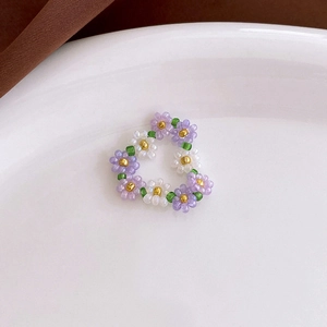 Detailed macro shot of handmade purple and white daisy bead rings in a heart layout