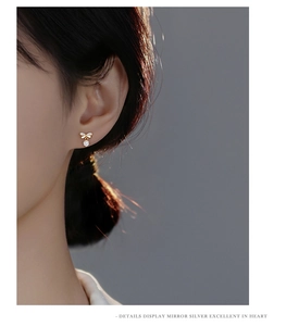 Close-up of golden S925 silver bow stud earrings with sparkling cubic zirconia on ear