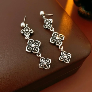 Detailed close-up of vintage silver clover earrings on a dark brown leather surface