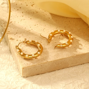 Detail view of gold-plated C-shaped earrings with embedded pearls on a textured background
