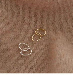 Orecchini a cerchio ovali lucidi in oro e argento su un caldo tessuto a maglia marrone
