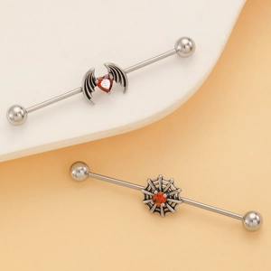 Detail of industrial barbell earrings with bat wings and spider web designs with red gems