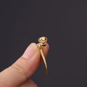 Detailed macro view of a golden snake stud earring with red eyes held by fingers