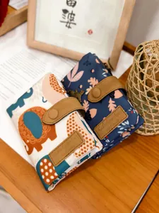 Close-up of canvas wallets with elephant and floral prints featuring leather snap buttons