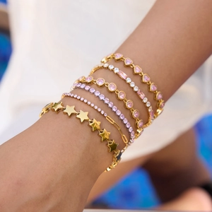 Detail of layered gold bracelets with pink zircon heart and star charms on wrist