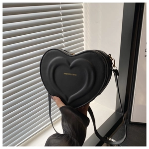 Detail of a heart-shaped black PU leather bag with gold text held against a shutter background