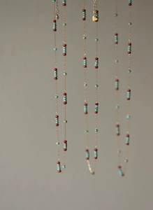 Detail of bohemian necklace featuring red and turquoise beads with gold heart charms