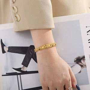 Detail of a gold rectangular geometric link bracelet styled on a fashion model's wrist