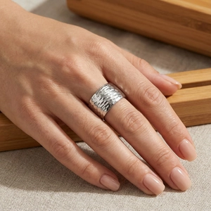 Close-up of a wide silver stainless steel ring with hammered texture on a hand