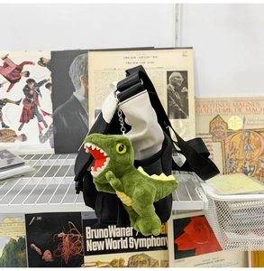 Green dinosaur plush keychain accessory on black and beige canvas messenger bag detail