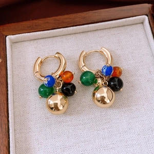 Détail de créoles dorées 18K avec des perles de pierre colorées dans un écrin en bois