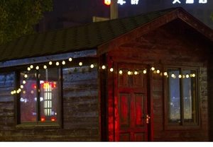 Detail of warm white G50 solar LED string lights decorating a rustic wooden cabin exterior