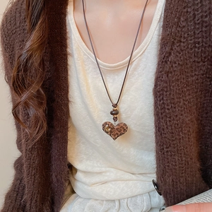 Close-up of leopard print heart pendant on a brown cord necklace worn by a model