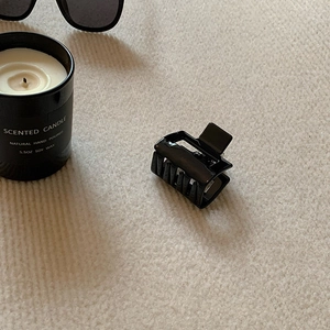 Close-up of a glossy black square hair claw clip on a textured beige fabric background