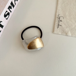 Detail of minimalist hair tie with white geometric charm and golden metallic accent
