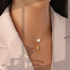 Gros plan d'un collier doré avec perle et pendentif carpe koi coloré sur un mannequin