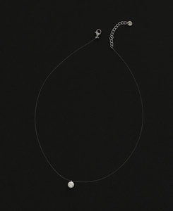 Detail of invisible necklace with round pearl pendant on thin wire and steel clasp