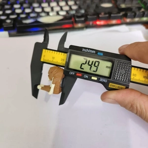 Digital caliper measuring the 24.9 mm width of a brown textured animal fridge magnet