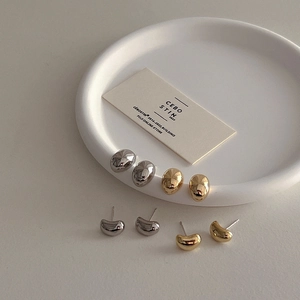 Minimalist gold and silver pebble studs on a white ceramic tray in macro view