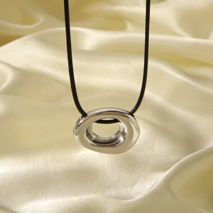 Detailed view of silver irregular oval pendant on black cord over silk fabric background